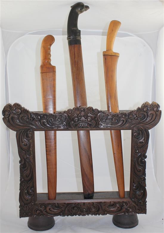 Indonesian carved wood dagger or sword stand, containing three Indonesian or Malaysian swords, early 20th century, longest sword 74(
